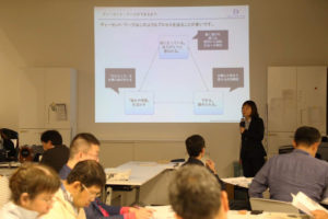 写真です。講師の中尾さんが、スライドを背景にして、皆さんに講義しています。